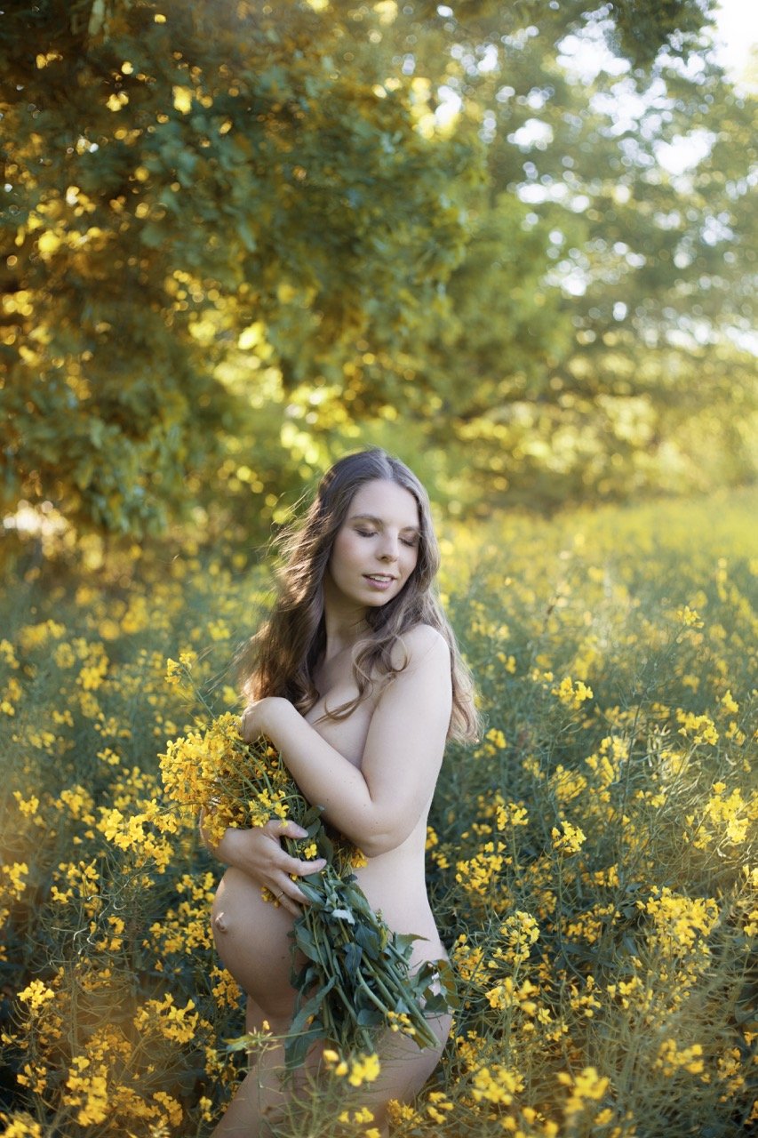 Frau in einem gelben Blumenfeld, Blumen haltend, mit Bäumen im Hintergrund.