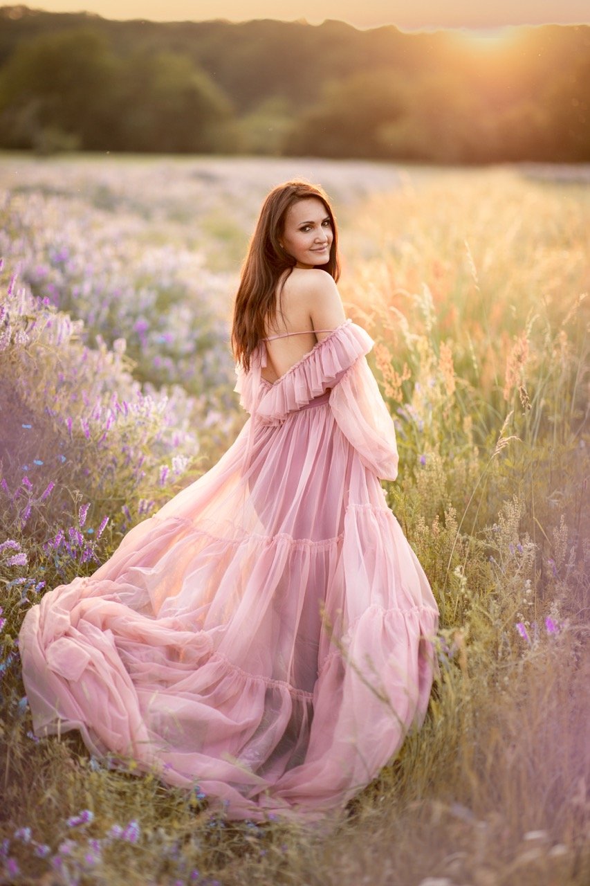 Frau in einem rosa Kleid steht auf einem Blumenfeld bei Sonnenuntergang.