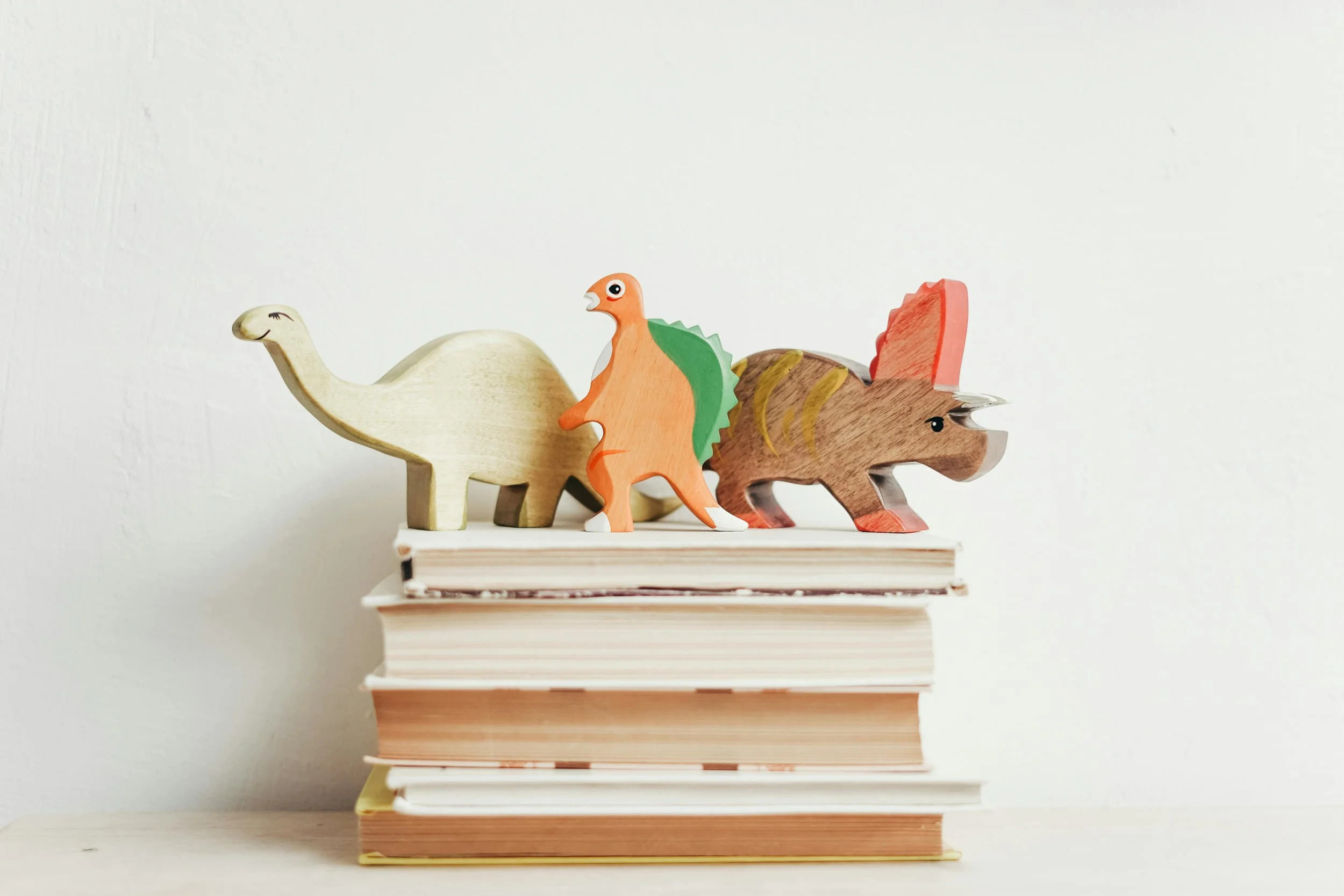 A stack of books with wooden dinosaur toys resting on top