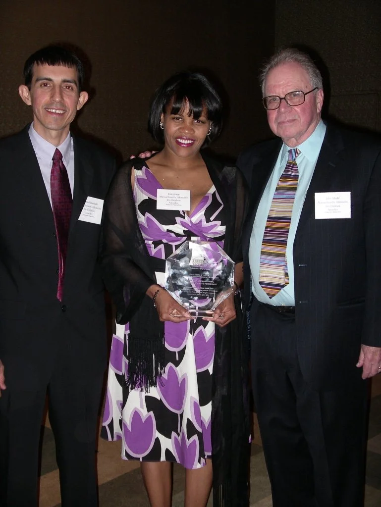Three people standing together at an award ceremony, with the woman in the middle holding a glass award.