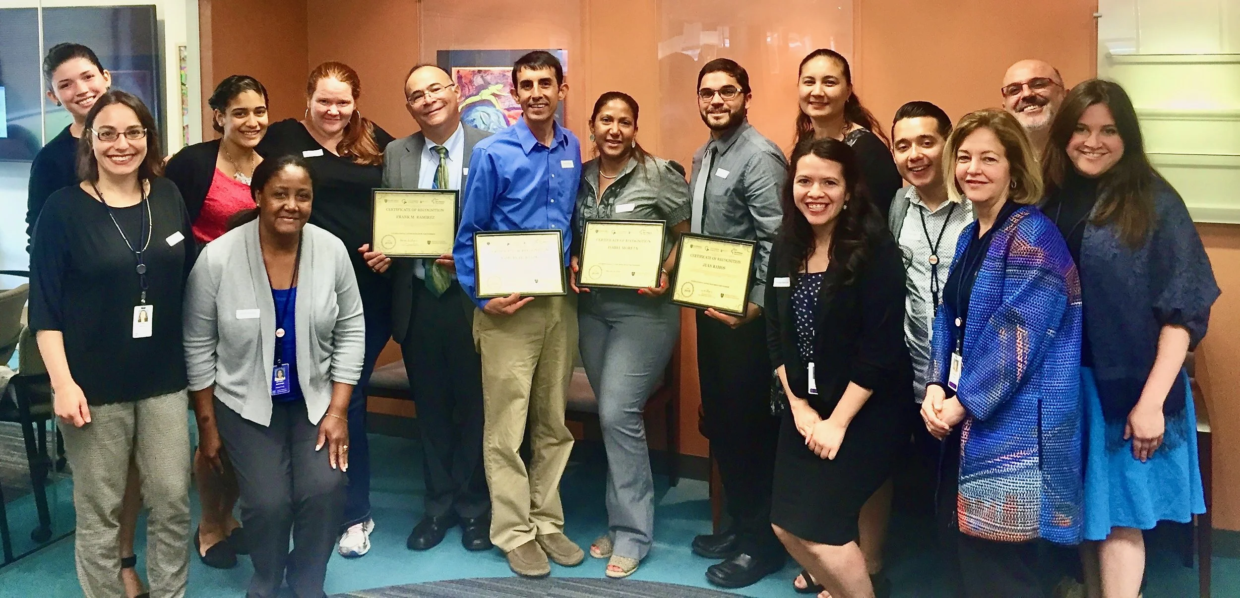 Group of people standing together indoors, some holding certificates, smiling for the photo.