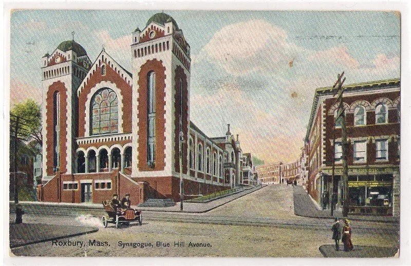 Vintage postcard of Blue Hill Avenue in Roxbury, Massachusetts, featuring a large synagogue with twin towers on the left and shops on the right, with people walking and a horse-drawn carriage in the foreground.