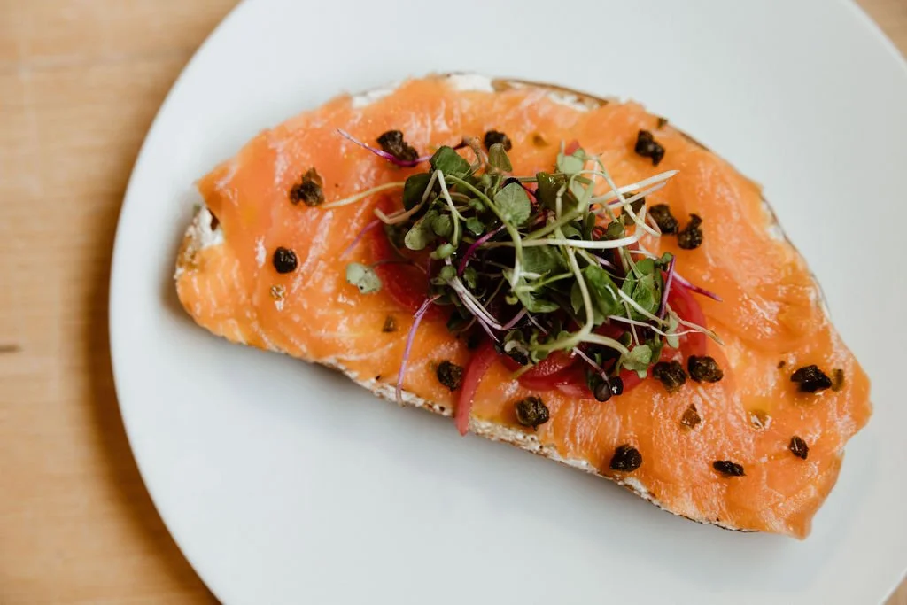 Open-faced salmon sandwich with capers and greens on a white plate.