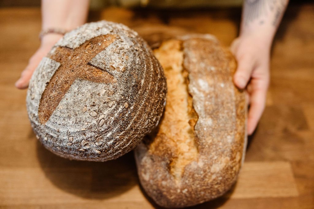 Person holding two loaves of artisanal bread on a wooden table.
