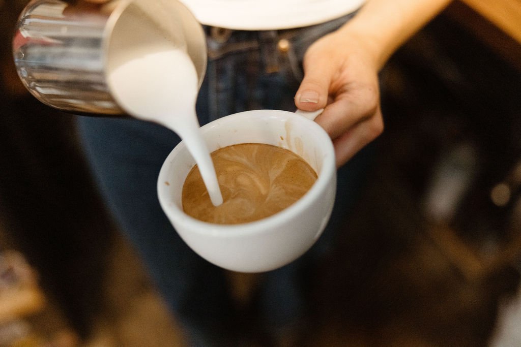 Person pouring cream into a cup of espresso, creating latte art.