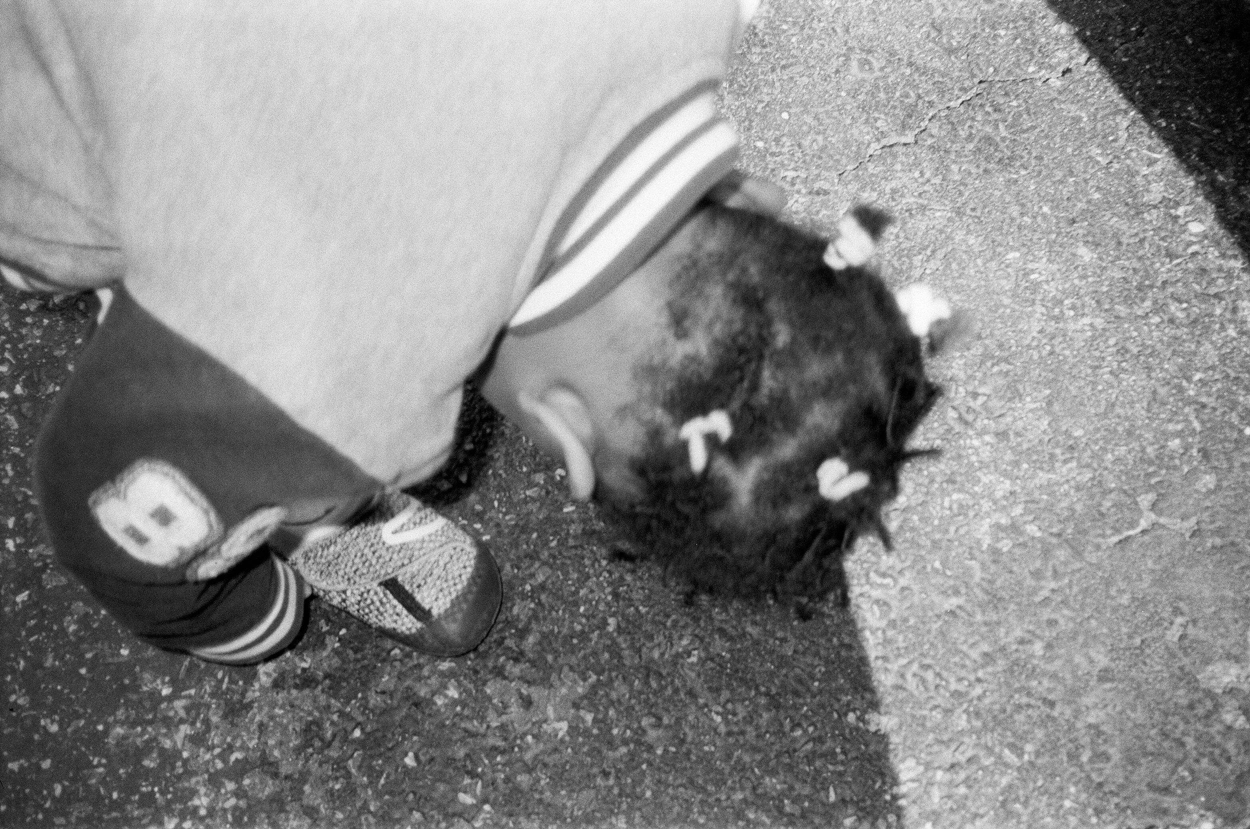 Black and white photo of a child bending down, wearing decorative hair ties and sneakers, with numbers on their pants.