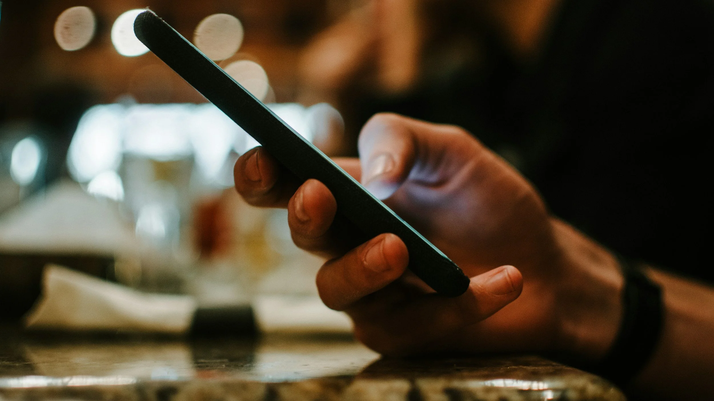 Close-up of a hand holding a smartphone in a dimly lit setting.