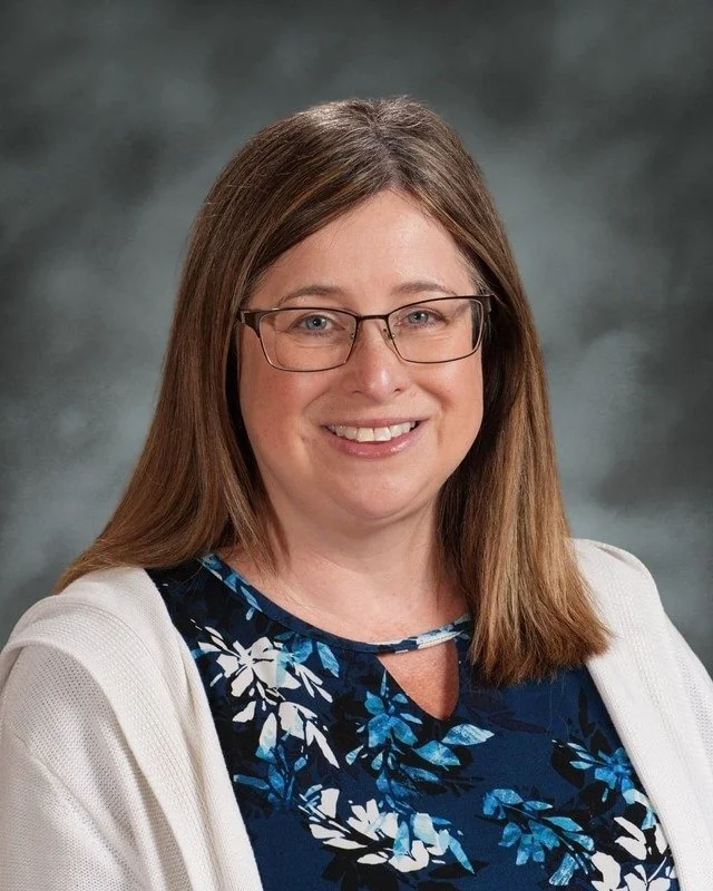 Smiling woman with glasses, wavy hair, and a star necklace