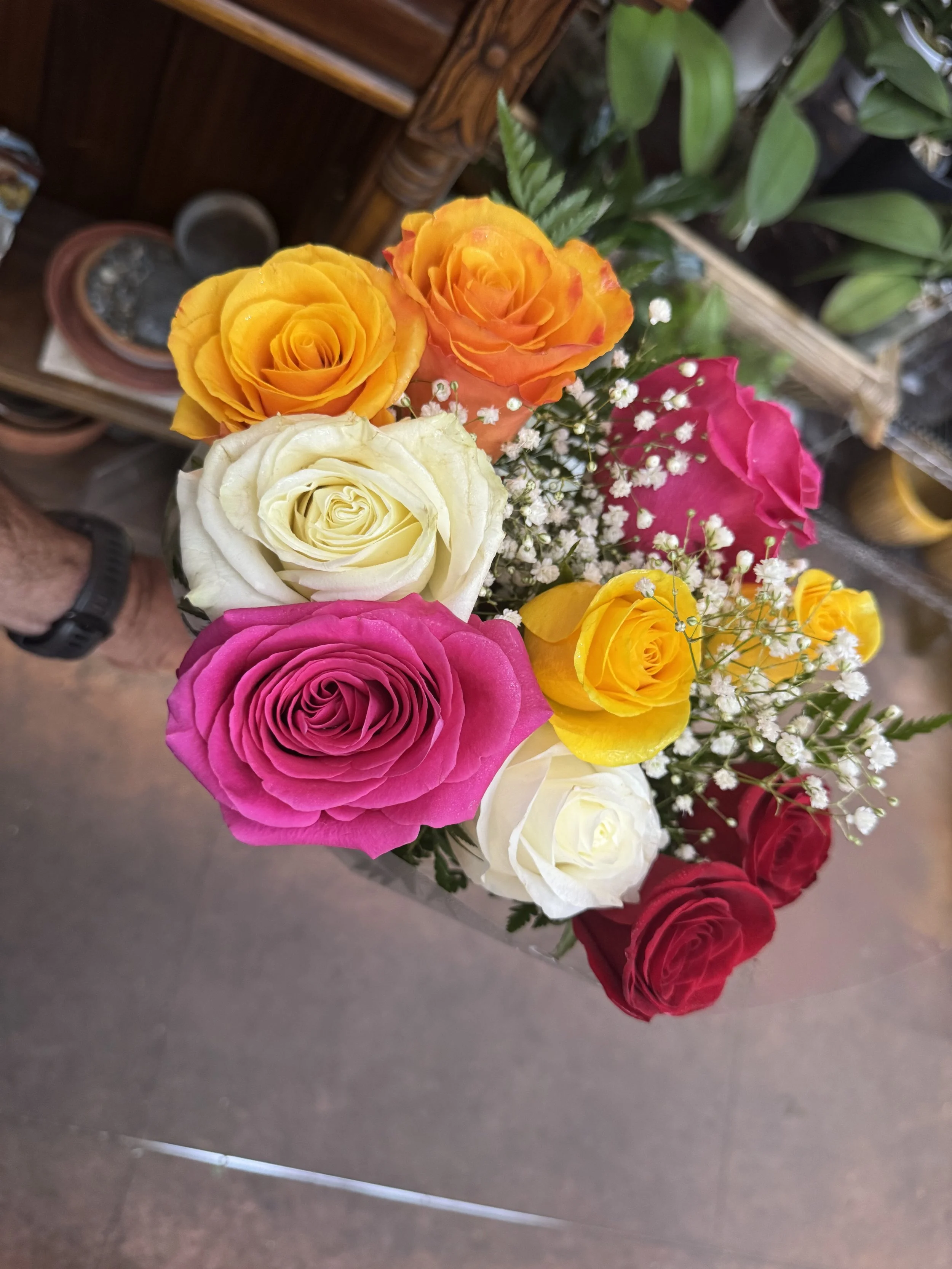 Colorful bouquet of roses including yellow, orange, white, pink, and red roses with small white baby's breath flowers.