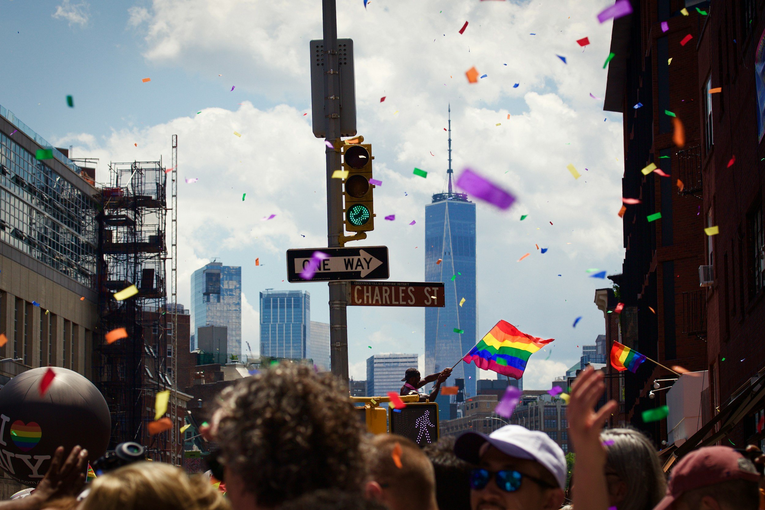 A joyful scene including a man waving a rainbow flag during the West Village Pride Parade.