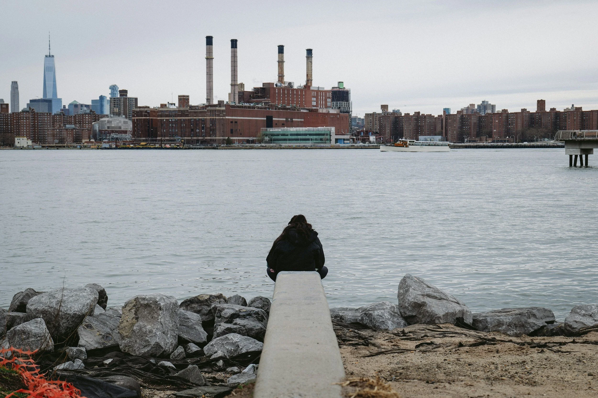 Person looking across the waterfront toward industrial buildings in the city.