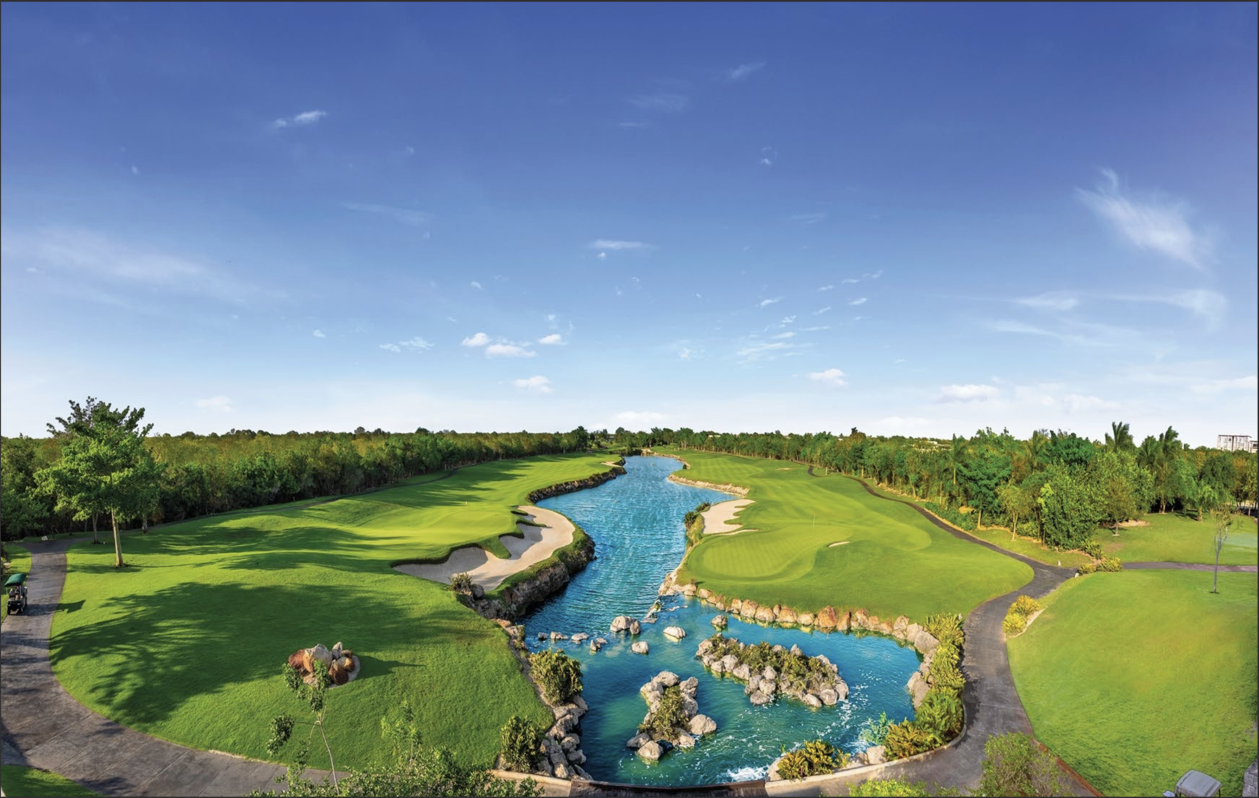 A scenic golf course with a narrow water feature running through the center, surrounded by manicured green grass, trees, and sand traps under a blue sky.