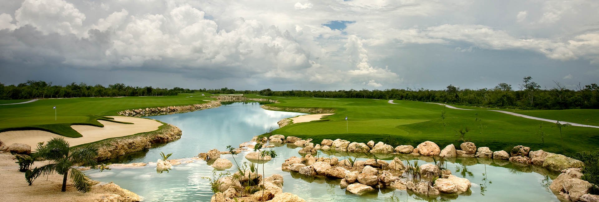 A scenic view of a golf course with a water hazard, sand traps, and green fairways under a cloudy sky.