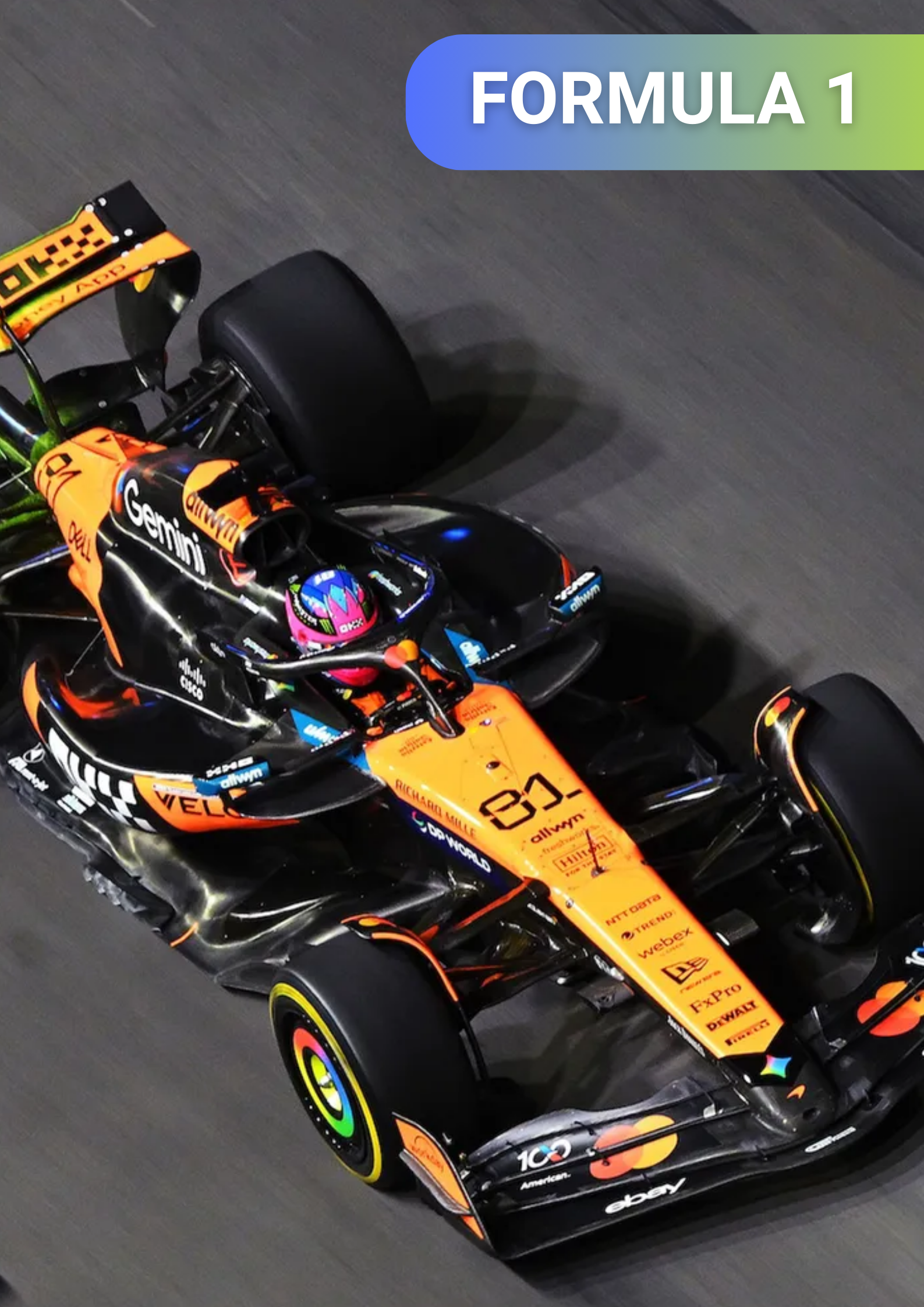 A race car on a track, predominantly black and orange, with various sponsor logos and the number 81 displayed on the front. The driver is wearing a pink helmet and the car is labeled 'Formula 1' in the top right corner.