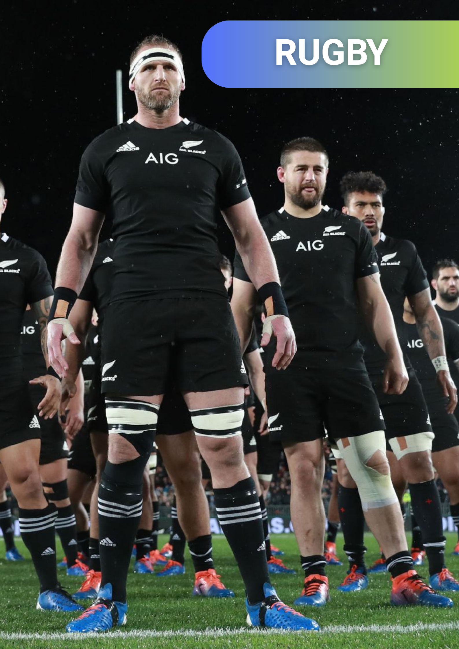 Rugby team standing on the field before a game, wearing black jerseys with the All Blacks logo and sponsor AIG, with some players wearing knee braces.
