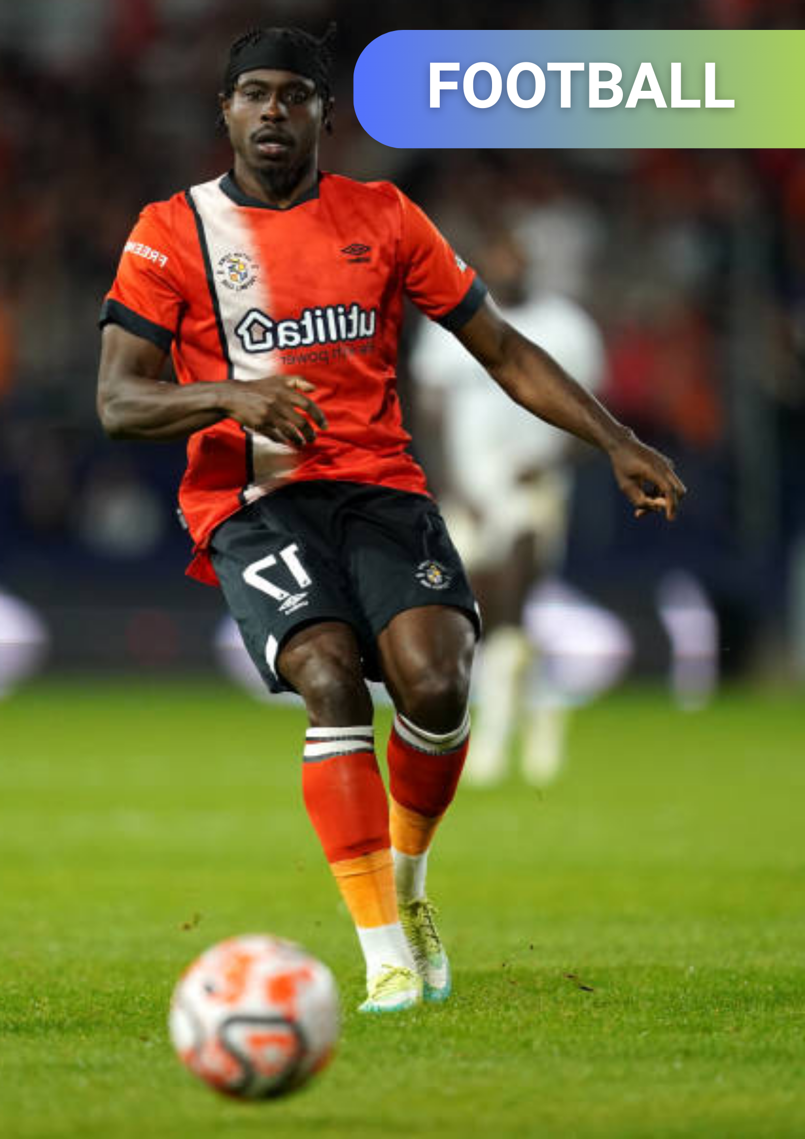 A soccer player in a red and black uniform with a multicolored sock on the left leg is on a soccer field, preparing to kick a ball, with a blurred crowd in the background.
