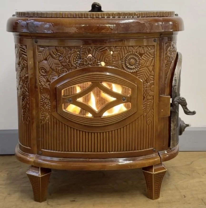 Wooden stove with carved floral and geometric patterns, casting warm glow through a decorative cutout window.