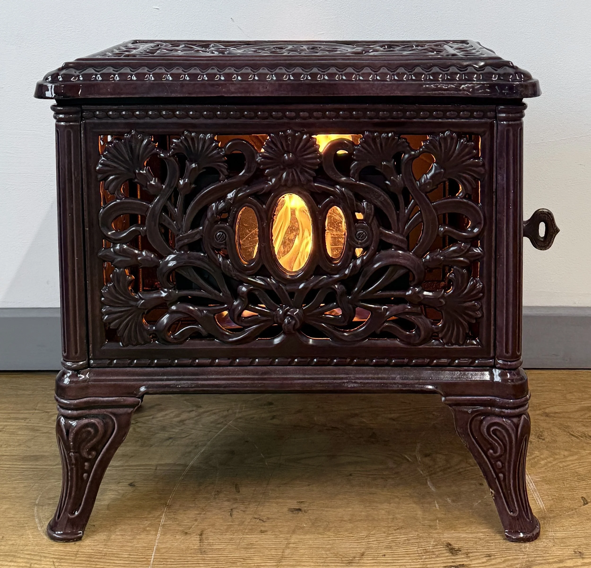 Dark carved wooden decorative box with intricate floral and vine motifs, with a glowing light inside, standing on a wooden floor against a plain wall.