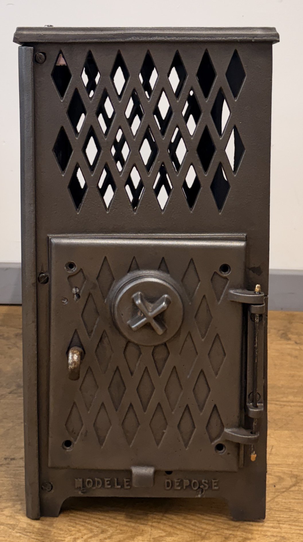 A vintage French stove with a diamond pattern design on the door, a circular locking mechanism, and a metal handle on the right side, labeled 'MODEL DEPOSE'.