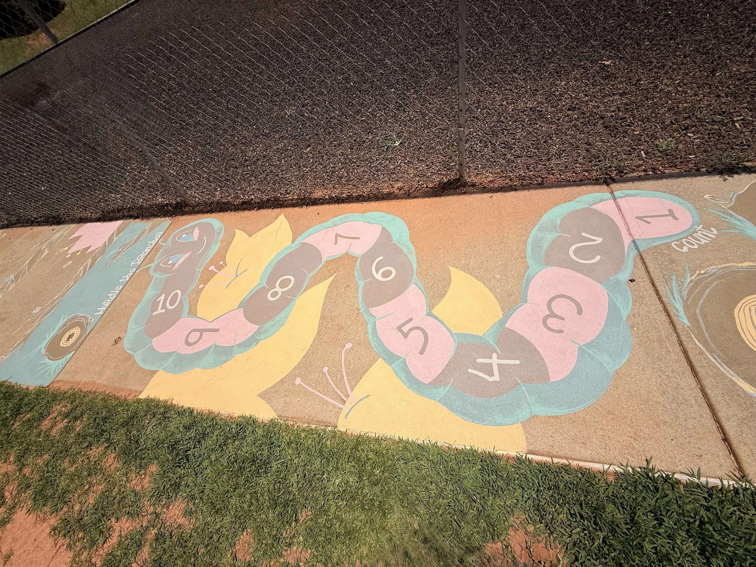 Colorful hopscotch game painted on sidewalk featuring a large yellow butterfly and a pink, blue, and gray caterpillar with numbered sections from 1 to 10.