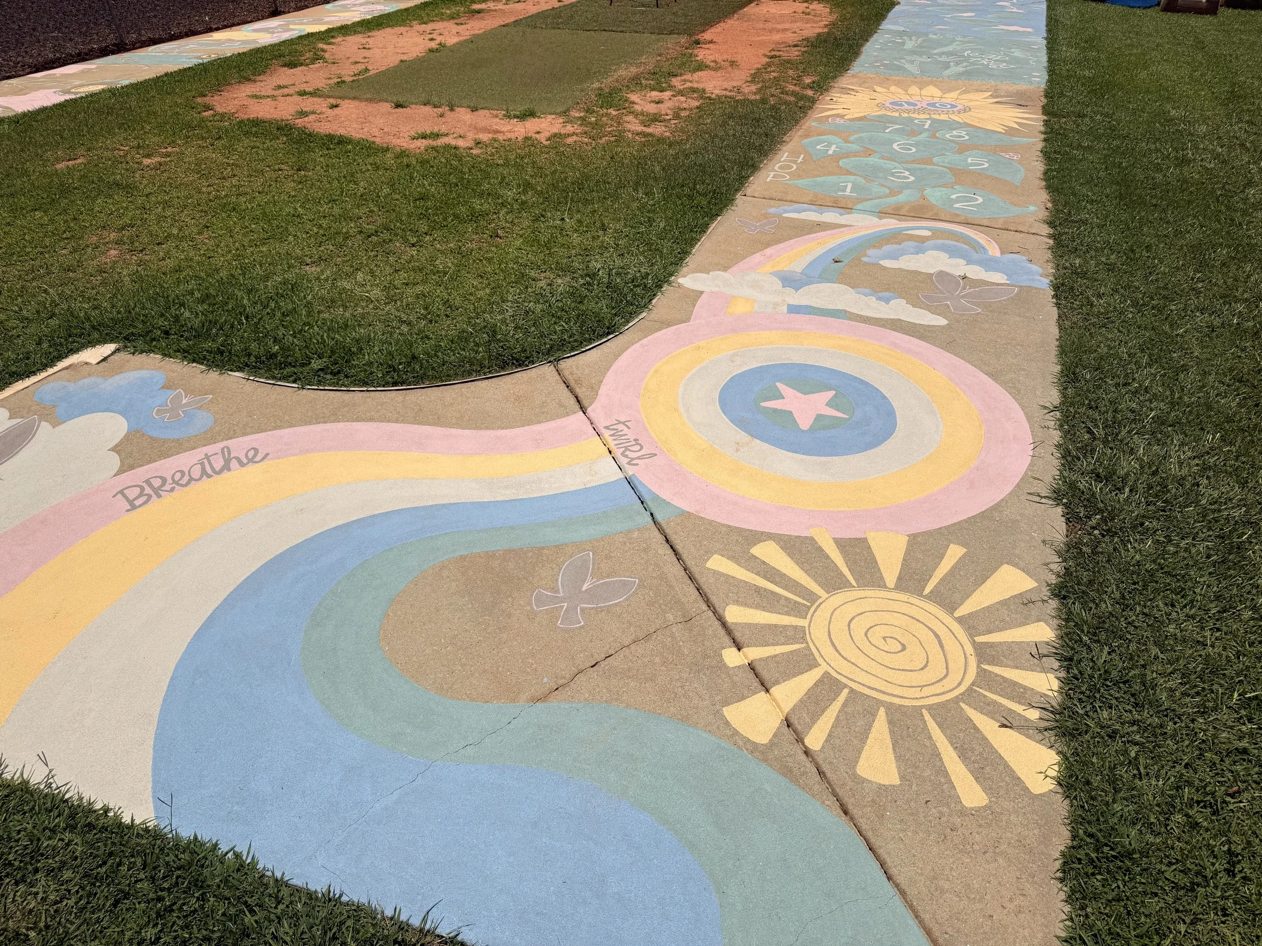 Colorful rainbow and sun painted on a sidewalk with clouds and butterflies, encouraging relaxation and positivity.