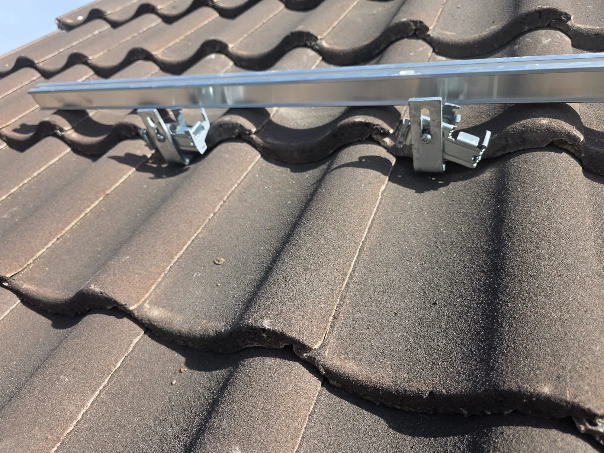 Close-up of solar panel mounting brackets on a tiled roof in sunlight.