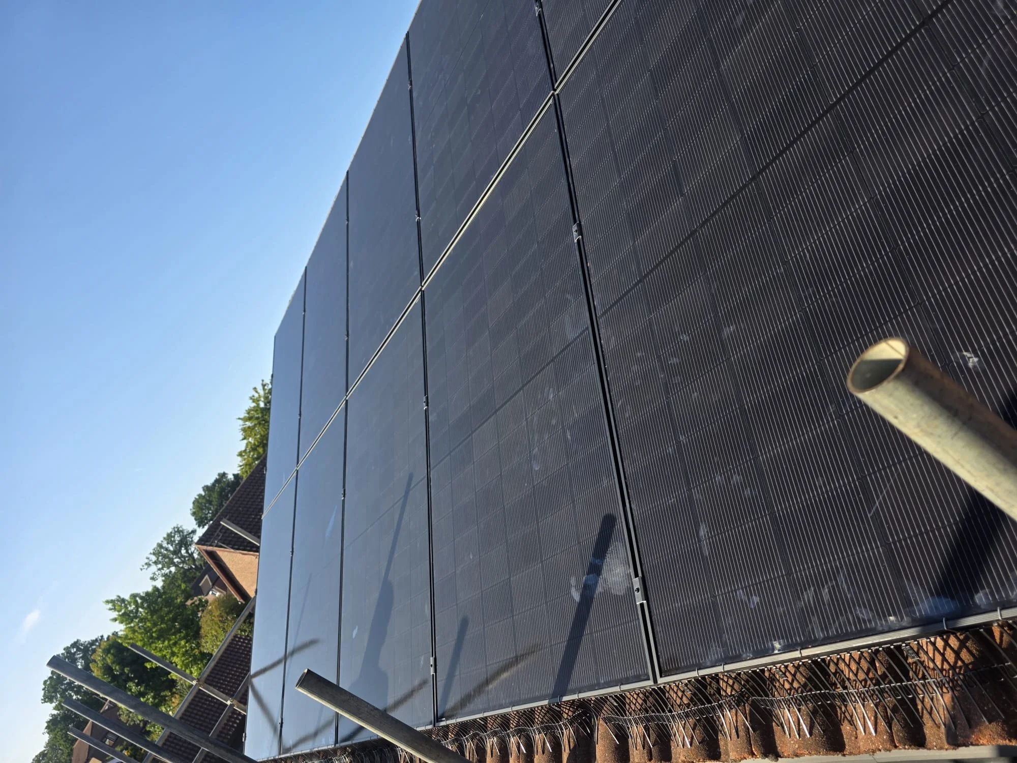A large array of black solar panels installed on a rooftop under a clear blue sky.