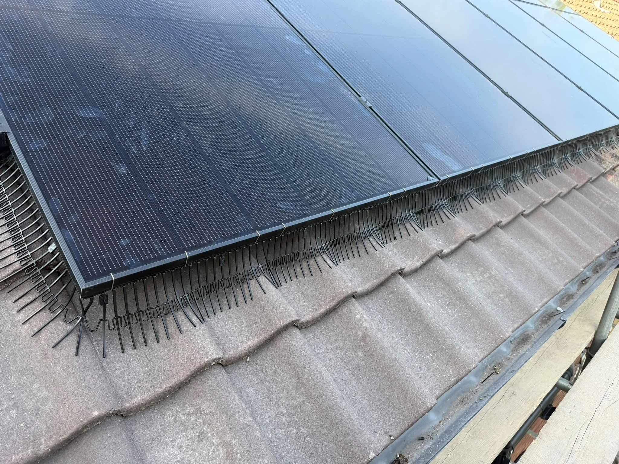 Close-up view of solar panels installed on a sloped roof with tiles, with wiring and metal framing visible.