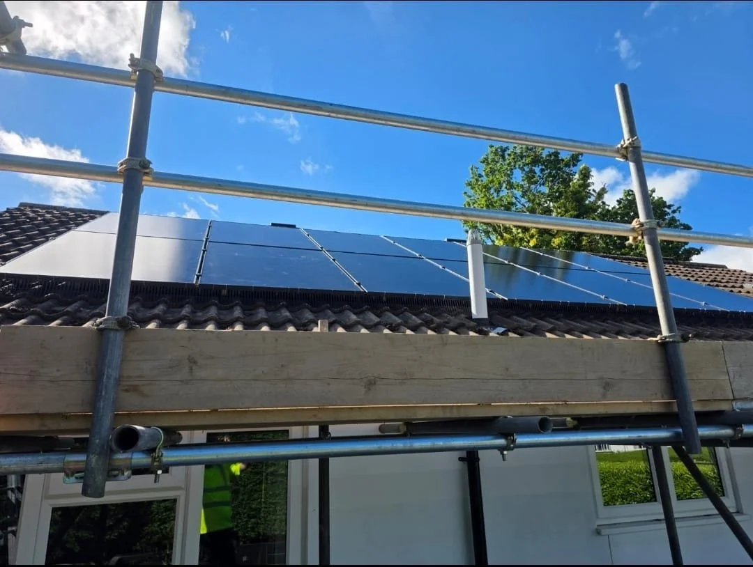 Solar panels installed on the roof of a house with blue sky and a tree in the background.