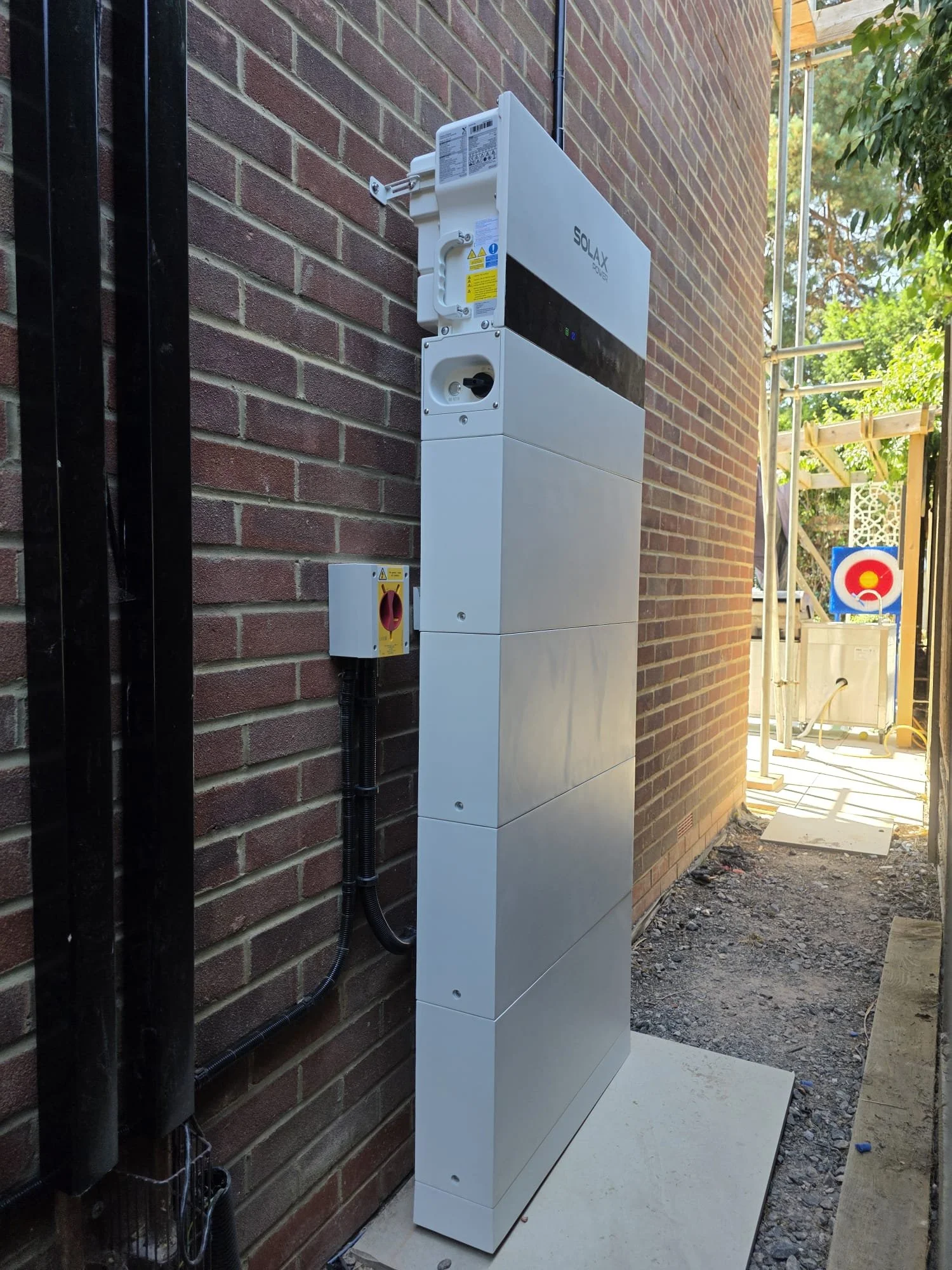 Cell tower equipment enclosure installed on an outdoor brick wall, with cables and construction area visible in the background.