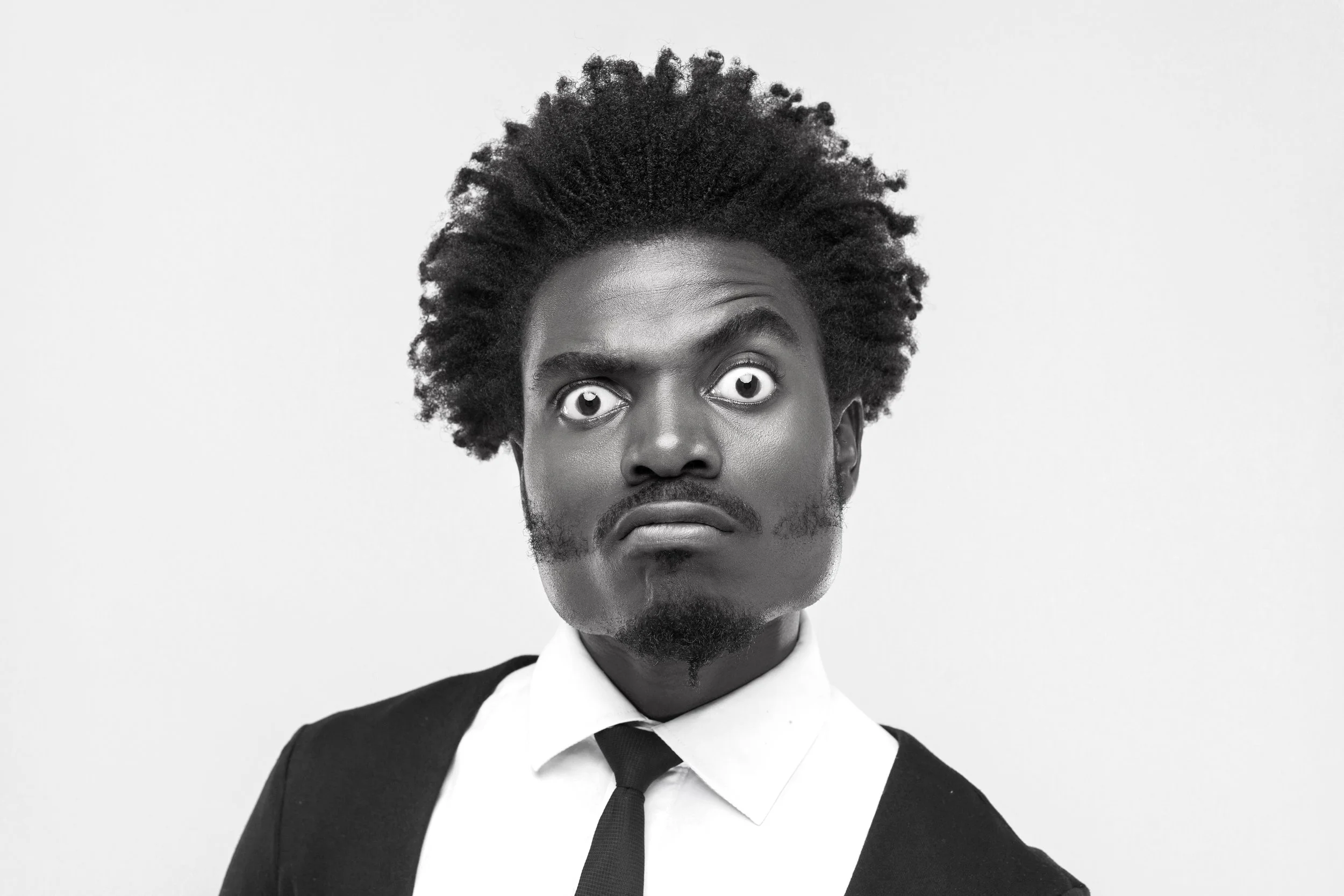 Black and white photo of a man with curly hair, facial hair, wide eyes, and a serious expression wearing a suit and tie.