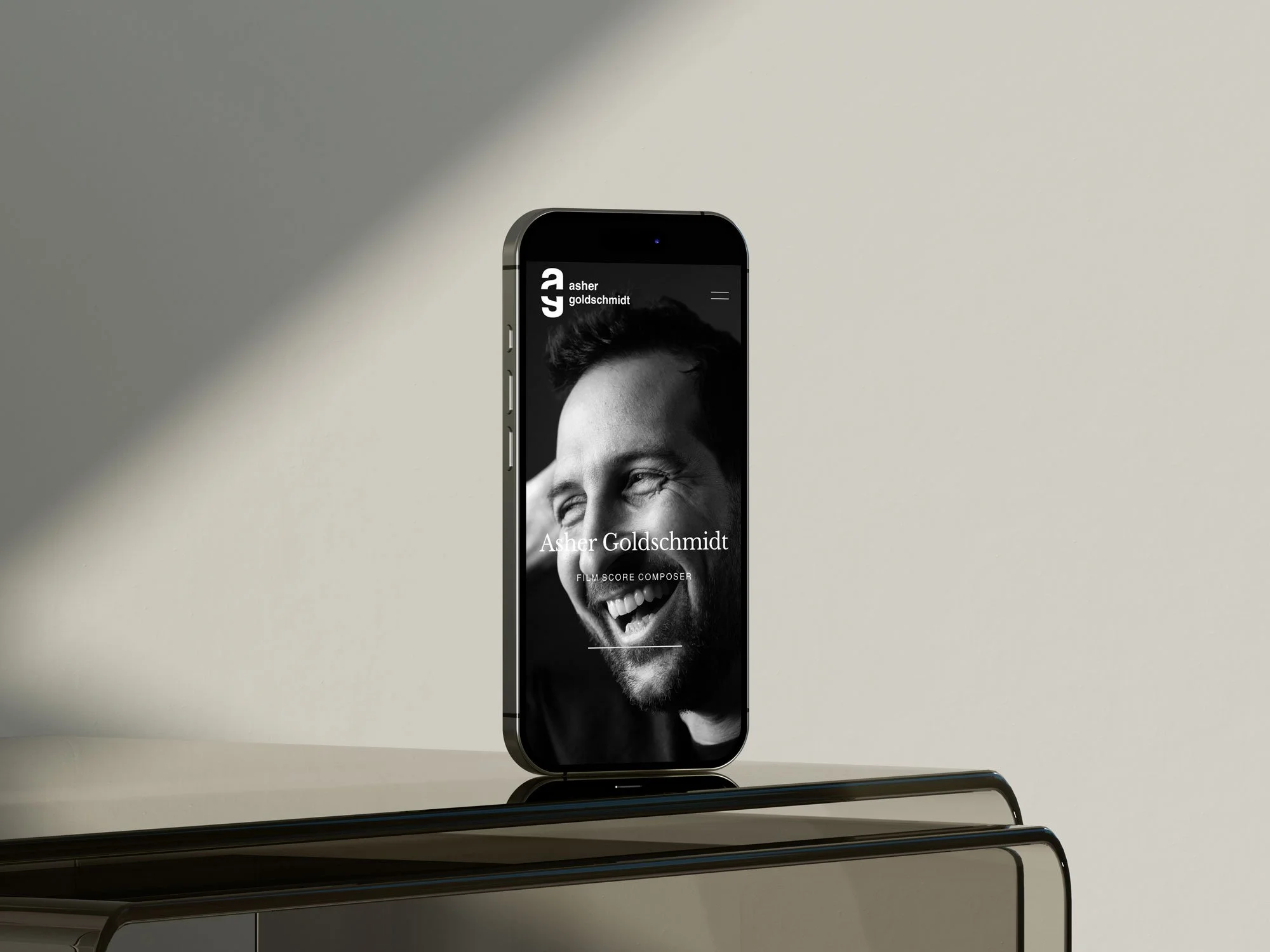 Smartphone displaying a black and white photo of a smiling man with curly hair on a minimalist table against a neutral background.