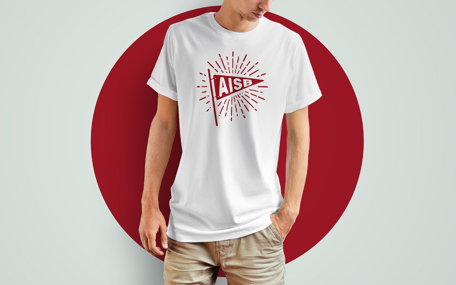 Person wearing white t-shirt with red "AISB" flag design, standing against large red circle backdrop.
