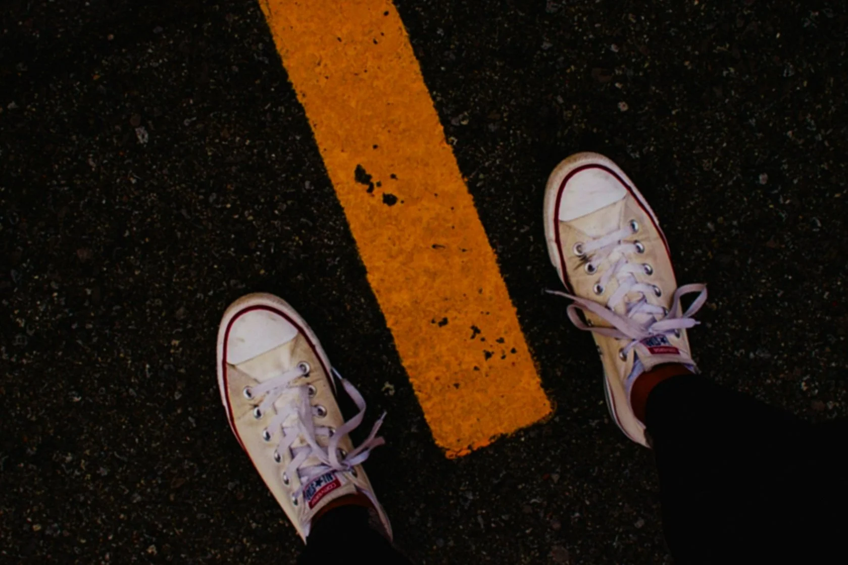 Person wearing white sneakers with pink accents standing on asphalt with an orange line.