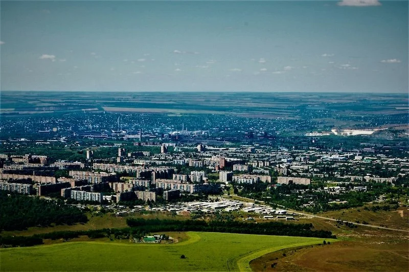 Aerial view of Crawley, West Sussex, with numerous apartment buildings and industrial areas, surrounded by green fields and open land, under a partly cloudy sky.