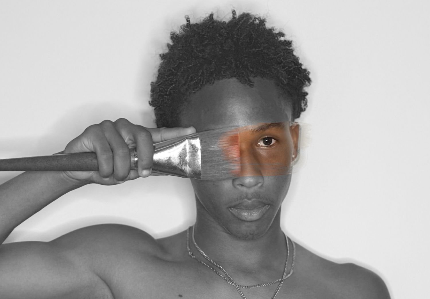 Black and white photo of Josiah Harris, known as Beranted, holding a paintbrush over one eye, adding color to the eye area.