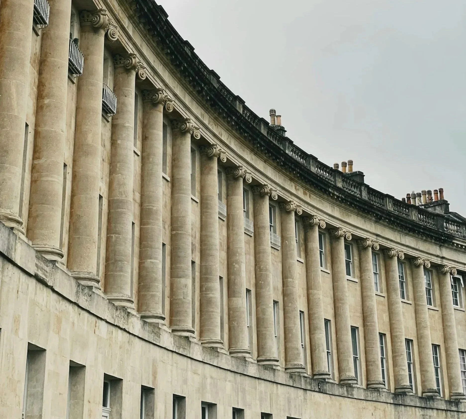 A classical building with tall, beige columns and small windows, topped by a black and white ornate balustrade and multiple chimneys, set against a cloudy sky, where a Treberys Private consultant advises a family.