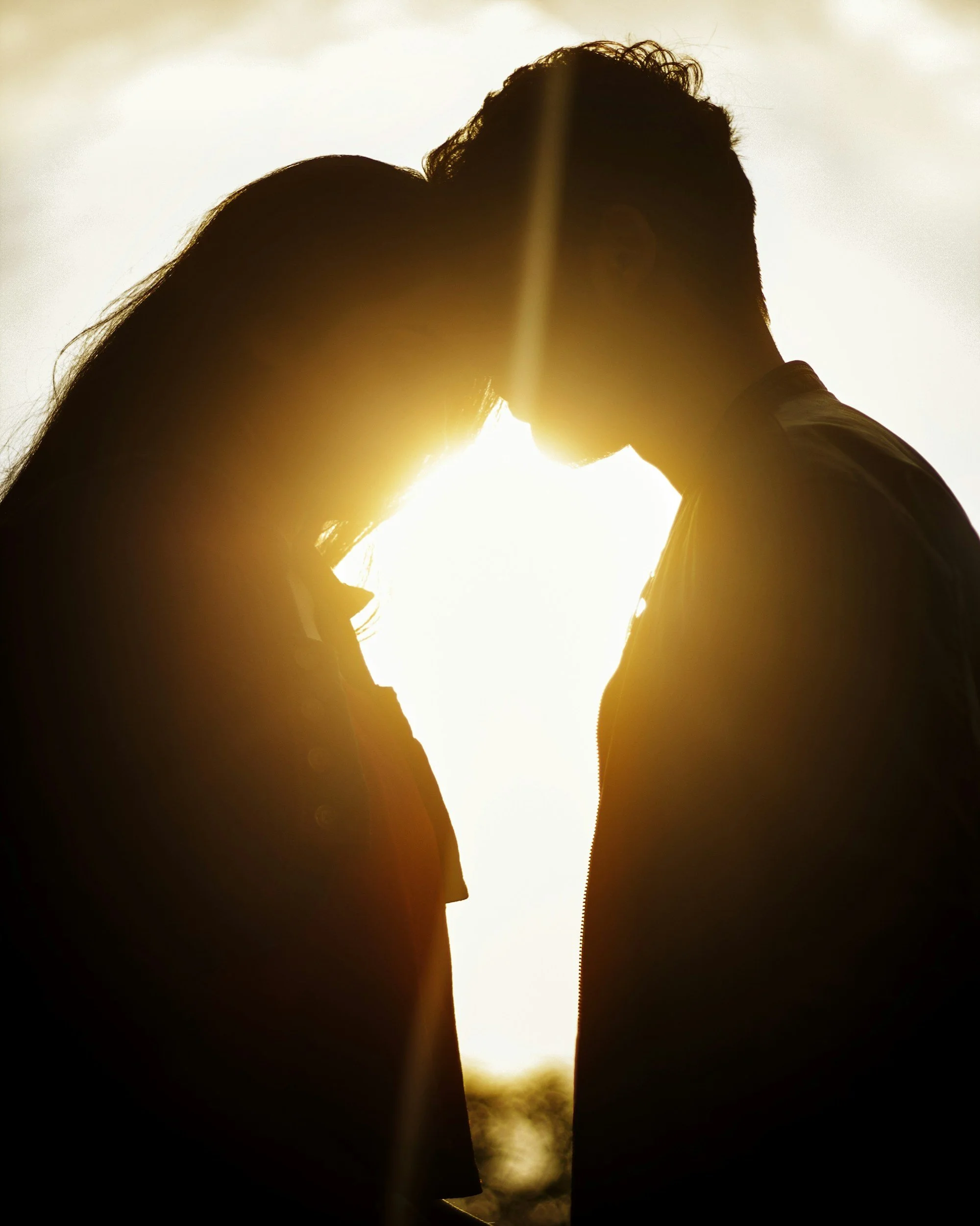 Silhouette of a couple with foreheads touching, backlit by the setting sun.