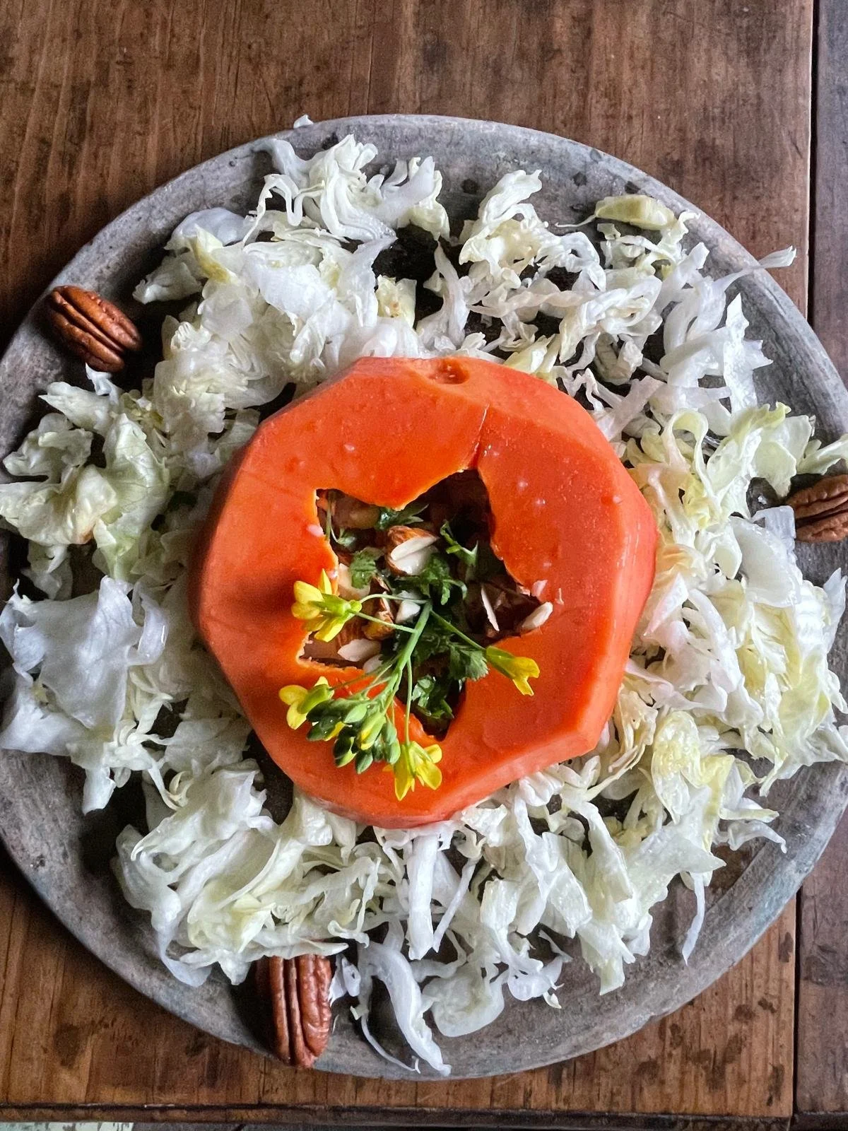 Un plato de enselada con adornos de flores y nueces sobre repollo rallado.