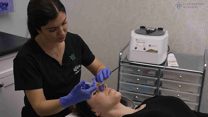 A woman receiving a facial treatment from a technician in a spa or clinic setting.
