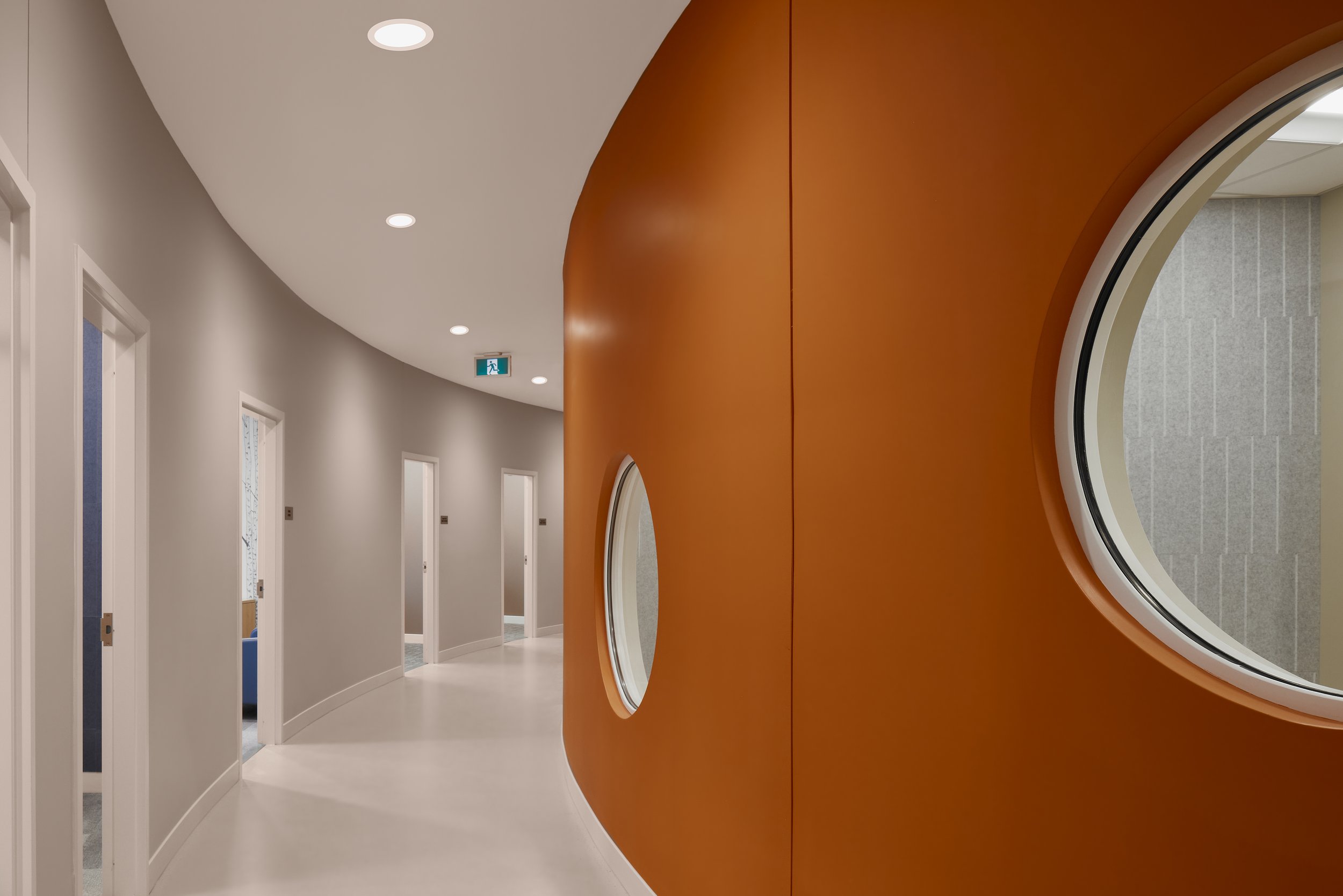 Modern hallway with white curved walls, multiple doors, and circular windows in a wooden wall.