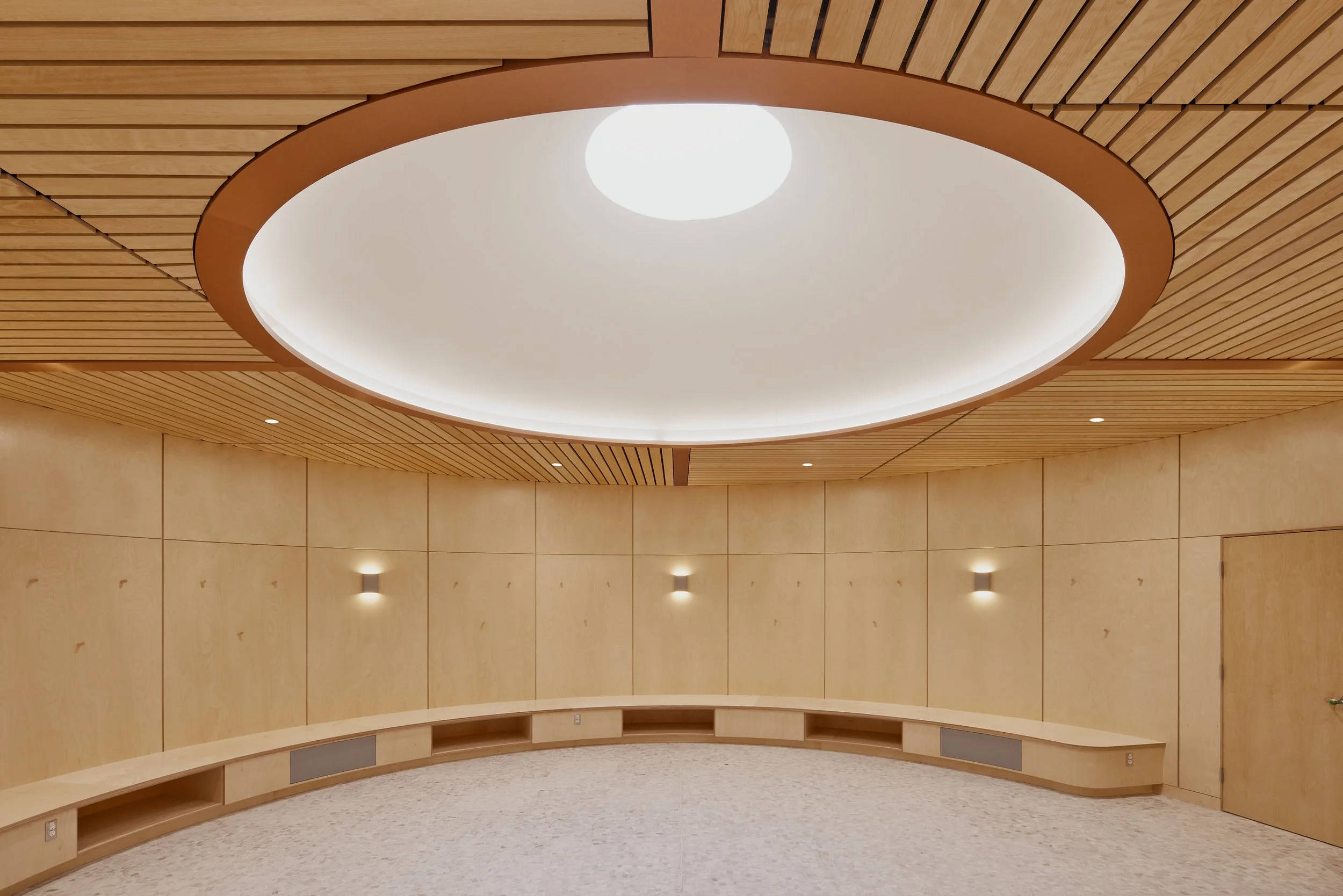 Interior room with wooden paneling on the ceiling and walls, a large circular ceiling light, and built-in wooden benches along the curved wall.