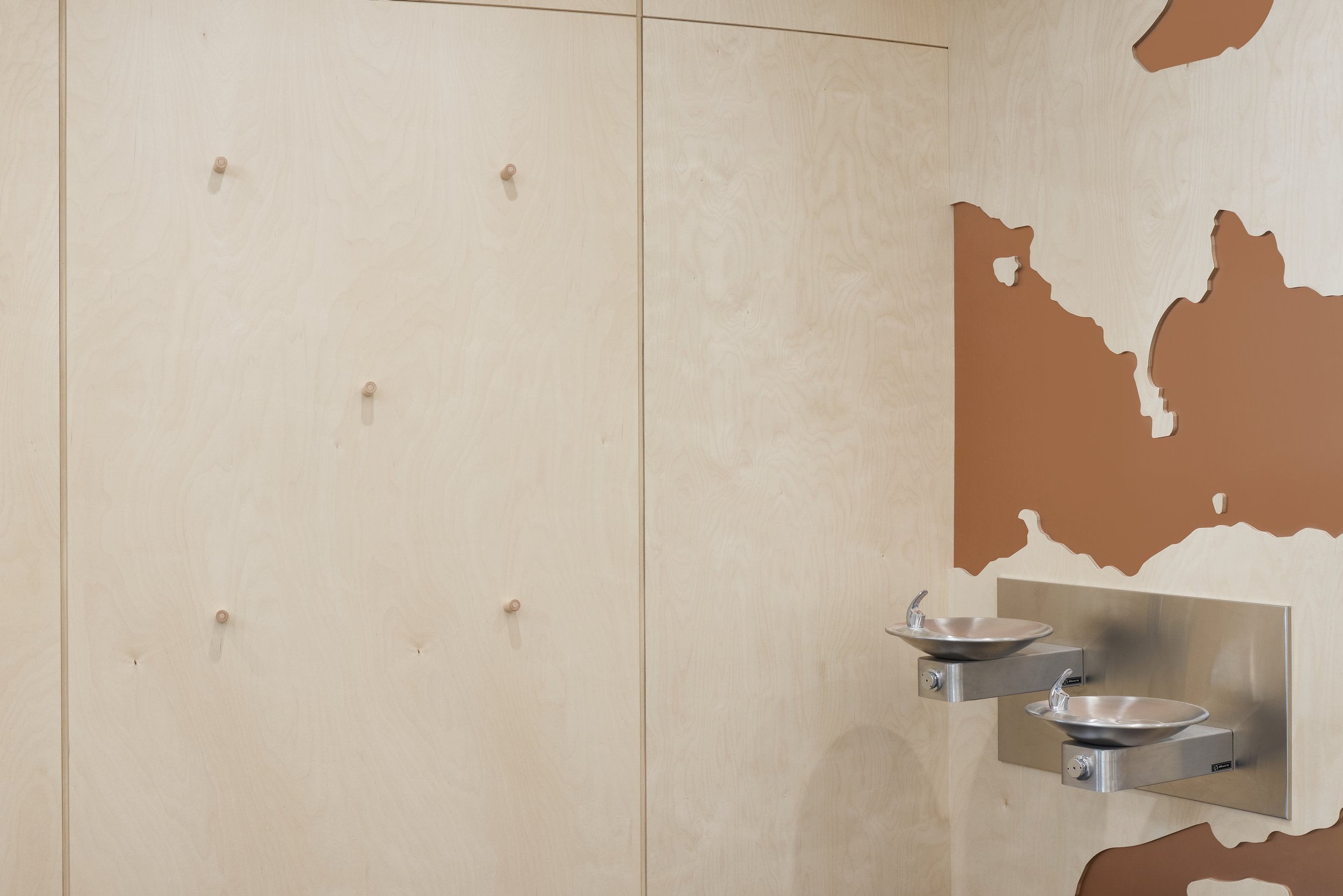 Two metal sinks attached to a wall with a painted map of Australia on a wooden wall.