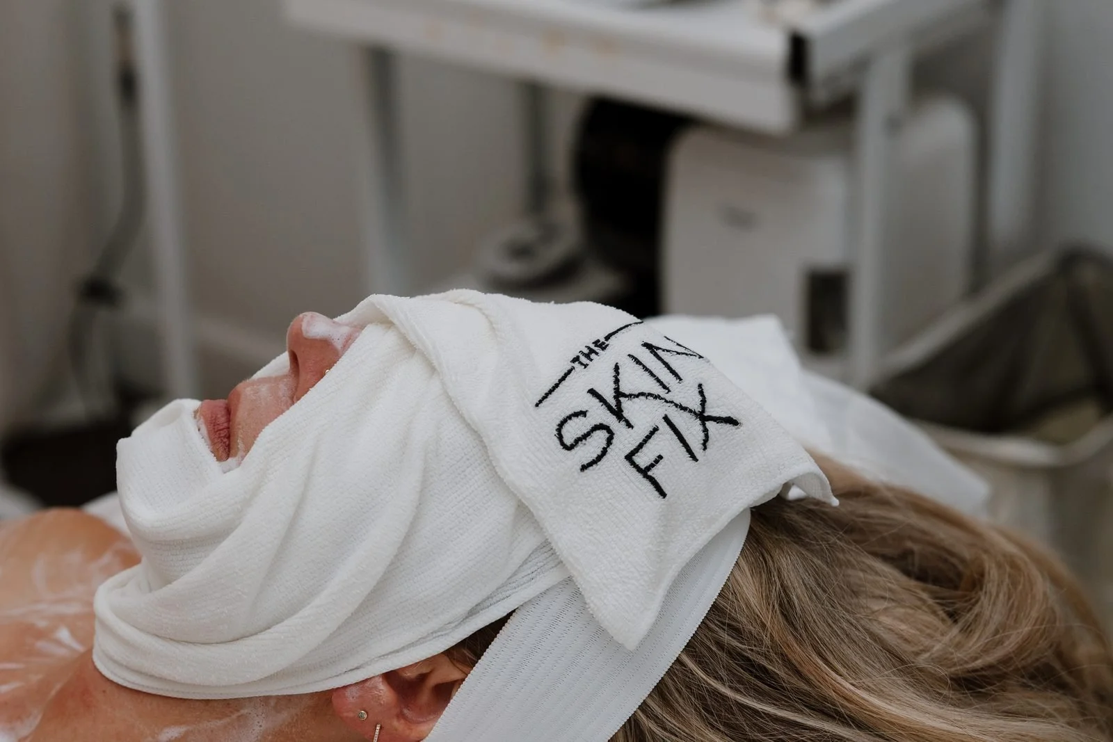 Client resting under a warm towel during a facial at THE SKIN FIX