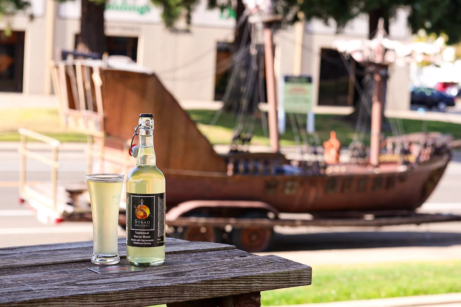 A bottle of mead sits on a picnic table with a small pirate ship parked in the background