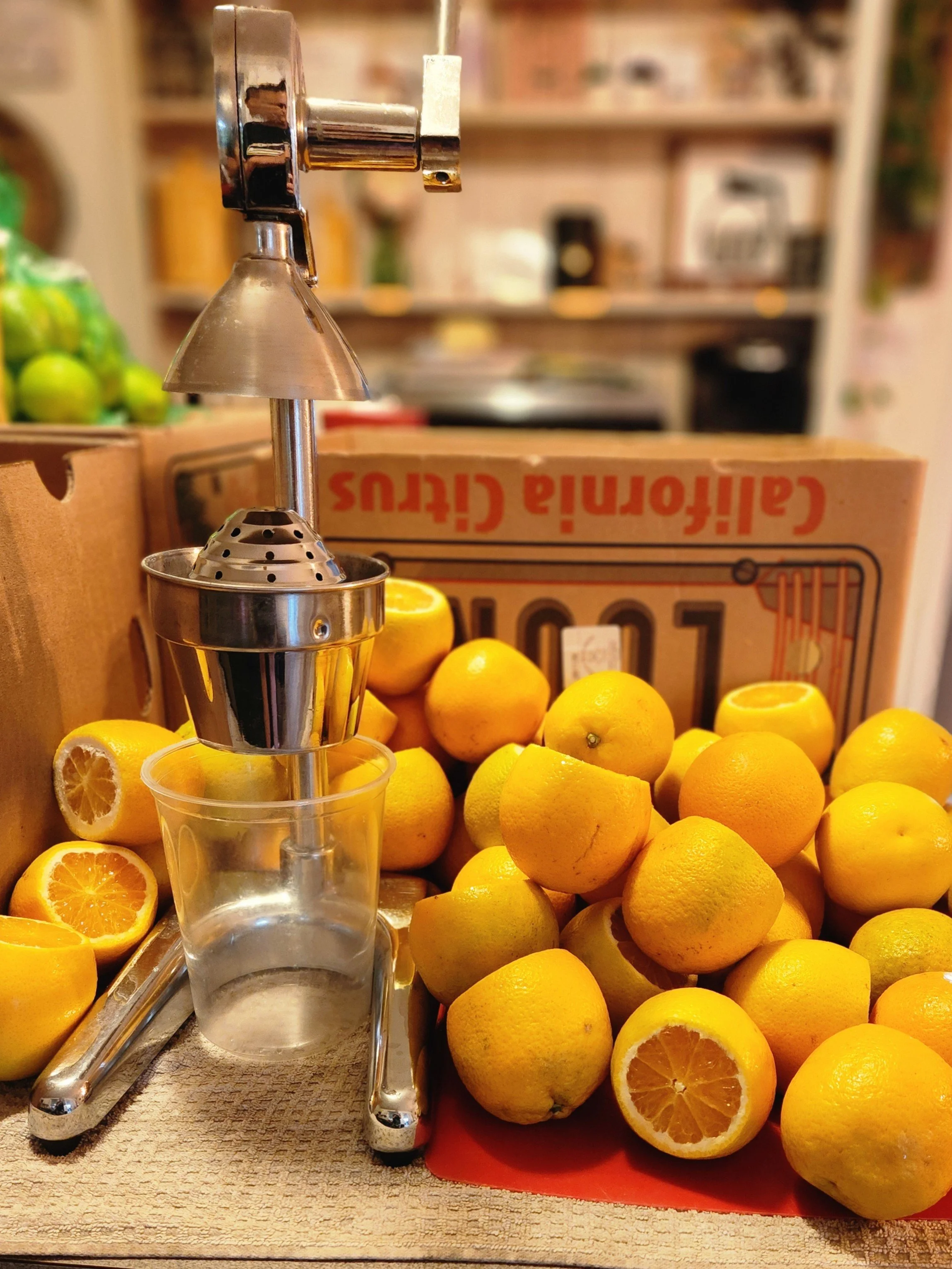 Lemon squeezer surrounded by fresh lemons, some whole and some cut in half on a wooden surface in a grocery store.