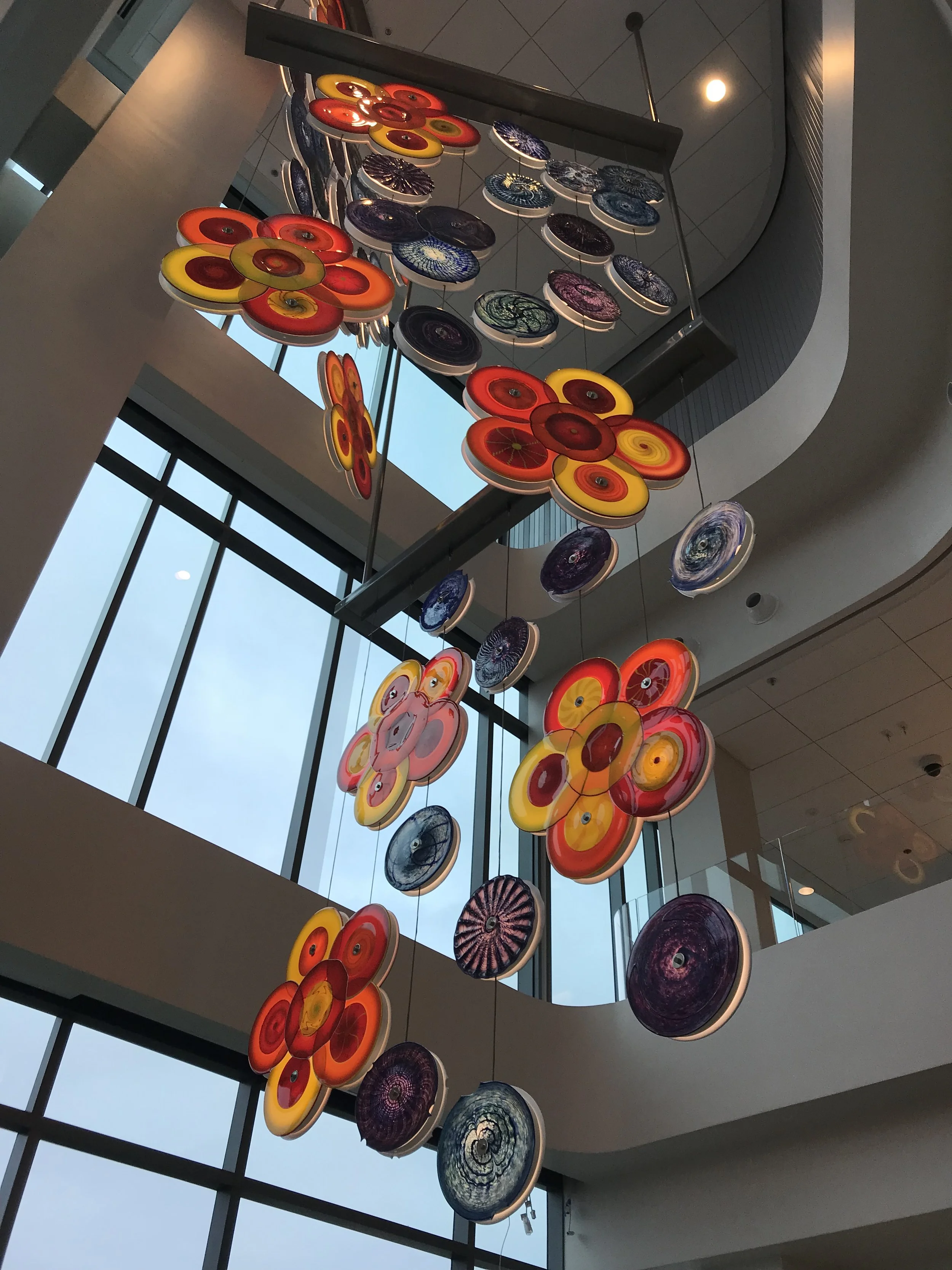 multi-story lobby art installation of suspended glassworks of orange and purple rondels