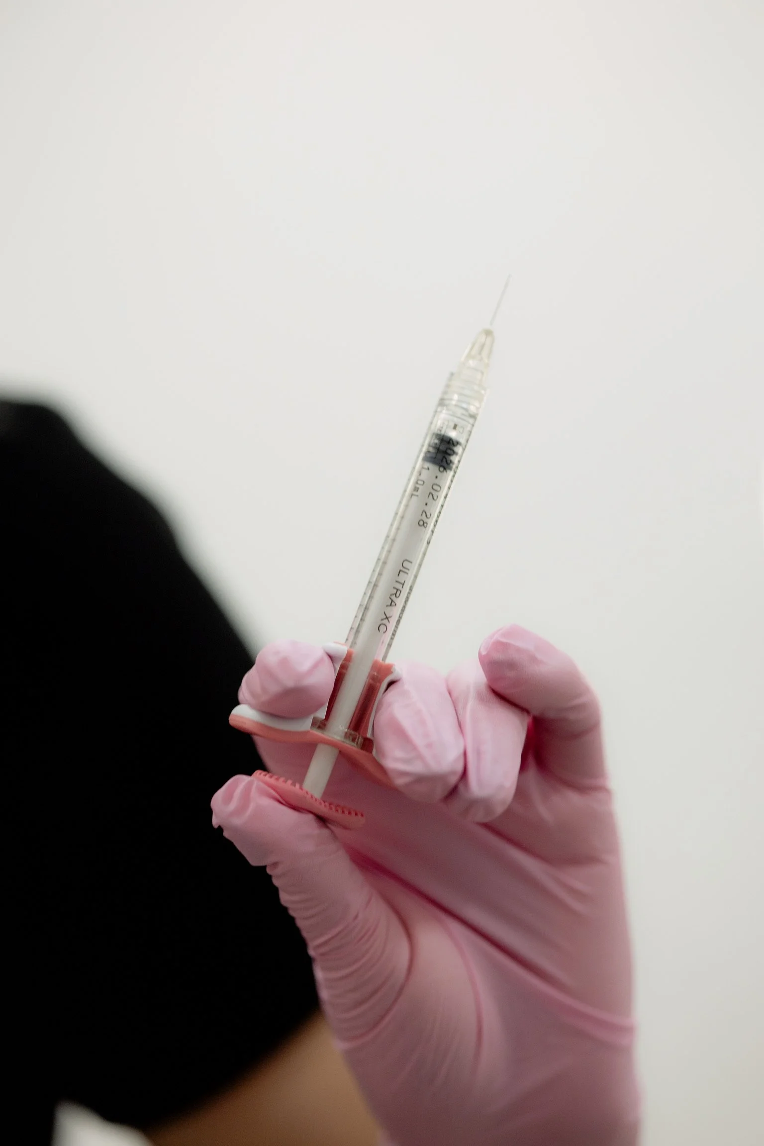 A hand wearing a pink glove holding a syringe.