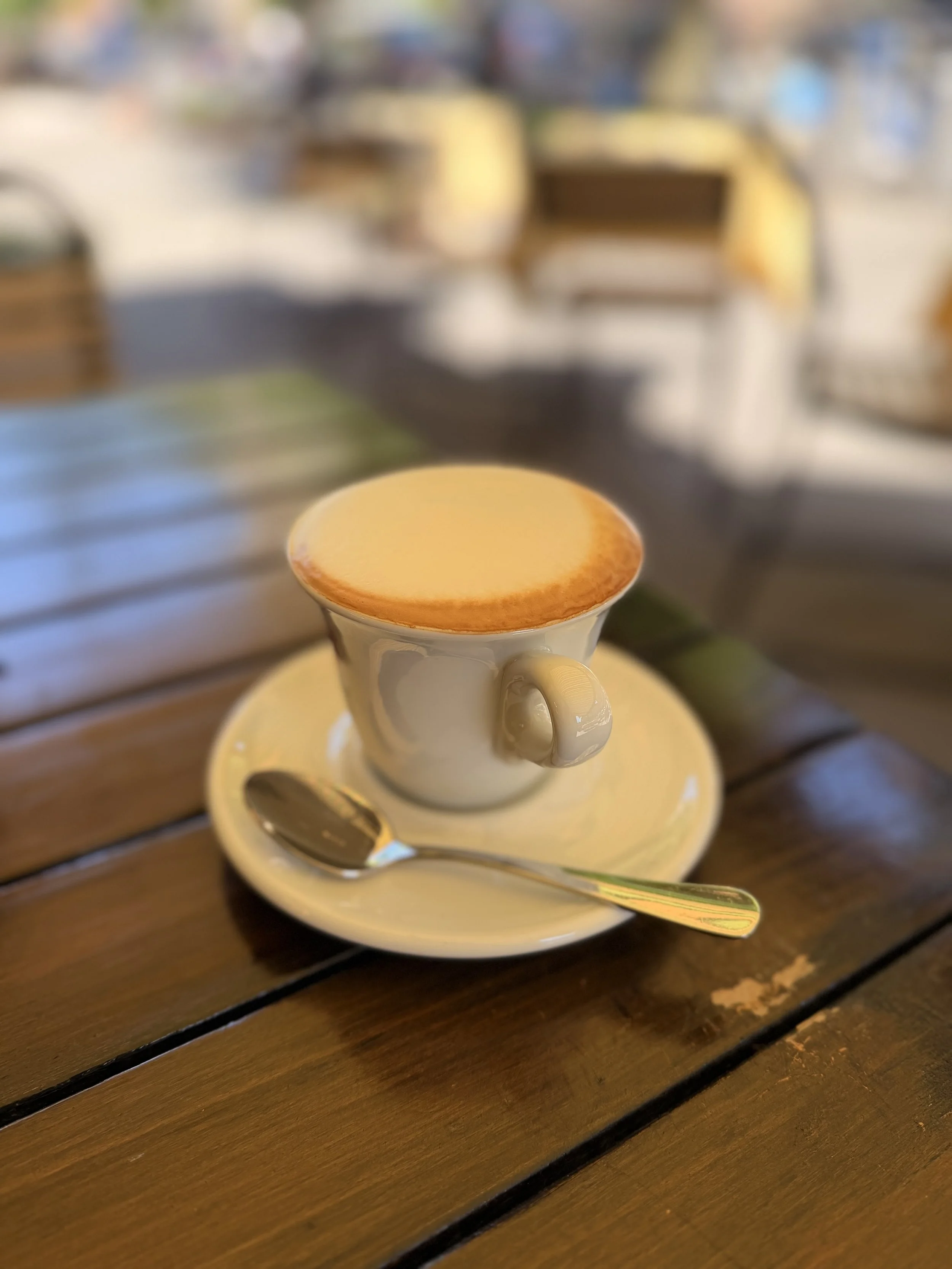 A frothy cappuccino, placed on a saucer with a teaspoon.