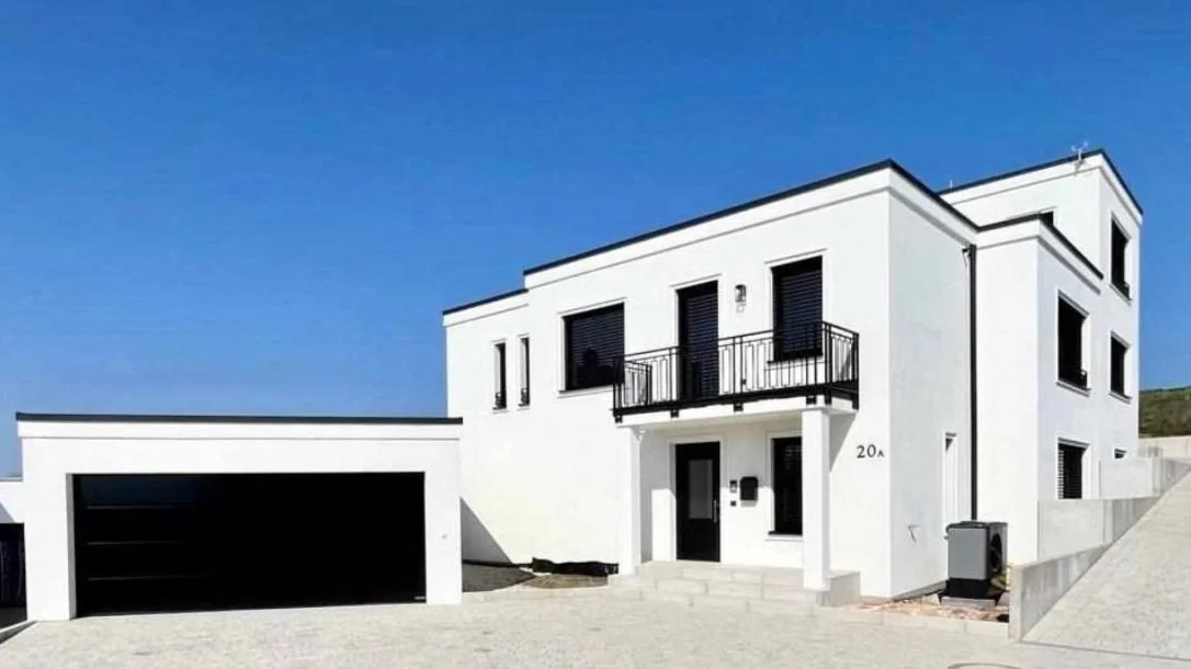 Modernes, weißes zweistöckiges Haus mit schwarzen Fensterläden, Balkon und Garage in sonnigem Himmel.